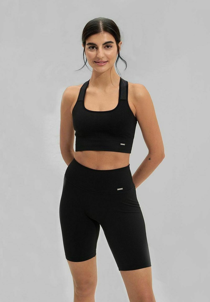 Černá sportovní souprava zahrnující krátký top se čtvercovým výstřihem a šortky s vysokým pasem, oboje s ribbovým texture a jemným brandingem.