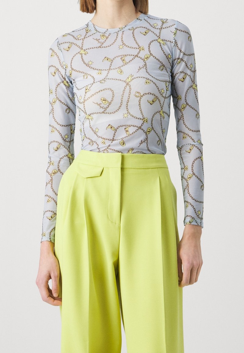 Pitkähihainen vaaleansininen paita, jossa on keltainen ketjumalli, yhdistettynä korkeavyötäröisiin, kirkkaan vihreisiin housuihin, joissa on tasainen vyötärö.