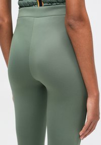 Ψηλοί ελιξίριοι ελαιοπράσινοι κολάν με λεία, ελαστική υφή. Χωρίς ραφές σχεδίαση που τονίζεται στη μέση και τους μηρούς.