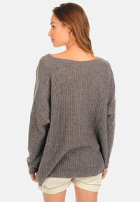 Pull gris à côtes amples avec un décolleté large et des manches longues, associé à un short léger, mettant en valeur un motif de tricot texturé.