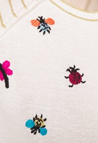 Suéter de punto con una base de color beige claro, adornado con insectos bordados en colores vivos: abejas, mariquitas y flores en rosa, azul y naranja.