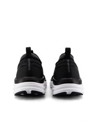 Svarta sportskor med ett texturerat tygöverdela, en dragflik och en vit mellansula med ett mönstrat svart yttersula.