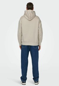 Felpa beige con cappuccio, dalla vestibilità comoda, orlo a costine e tessuto testurizzato. Abbinata a jeans denim blu larghi e sneakers nere.