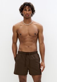 Braune Badeshorts mit elastischem Taillenbund und Kordelzugdetails, die einen strukturierten Stoff und eine entspannte Passform aufweisen. Keine sichtbaren Taschen.