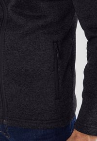 Chaqueta de cierre en color gris oscuro con una tela texturizada. Presenta un bolsillo lateral con cremallera y un ajuste ceñido en las mangas. Color sólido, sin patrones.