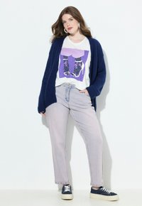 Cardigan lavorato a maglia blu navy sopra una maglietta bianca con una grafica viola e stivali floreali, abbinato a jeans di denim chiaro e sneaker blu navy.