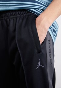 Sorte træningsbukser med elastisk talje, der har en sidelomme, grå detaljer og Jordan-logoet broderet i grå på benet.