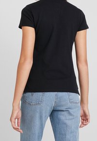 Svart kortärmad t-shirt, bomullsmaterial, åtsittande form, rund hals, enkel design, tillsammans med ljusblå högmidjade jeans, visande bakvy.