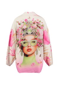Blusa ligera y oversize con un colorido estampado de flores, adornada con una mujer que lleva gafas. Los colores incluyen crema, rosa y verde.