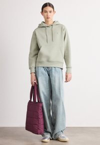Lys grønn bomullhettegenser med snor, frontlomme; sammen med løse, falmede blå jeans. Holder en quiltet burgunder veibag.