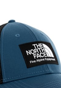 Kék szövet sapka fekete hálós panellel. Az elején hímzett fehér logó pillangó látható, amelyen a következők olvashatók: "THE NORTH FACE" és "Fine Alpine Equipment."