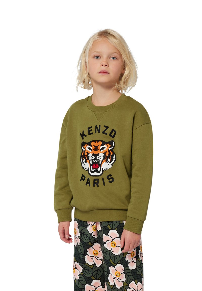 Felpa verde oliva con logo KENZO PARIS e grafica del tigre ricamata. Abbinata a pantaloni con motivo floreale caratterizzati da fiori rosa e foglie verdi.