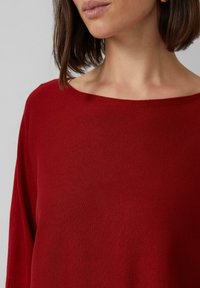 Roter Strickpullover mit weiter Bootsausschnitt und langen Ärmeln, der eine glatte Textur und einen lässigen Schnitt aufweist.