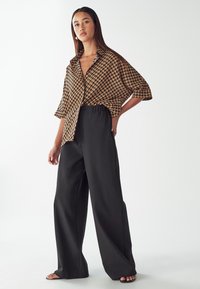 Brązowa i czarna koszula z krótkim rękawem w wzory, z kołnierzykiem, połączona z luźnymi czarnymi spodniami. Gładki materiał i swobodny krój.