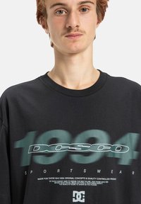 Čierne bavlnené tričko s brandom "DC" v zelenej farbe, s textom "1994" a "SPORTSWEAR". Klasický okrúhly výstrih a pohodlný strih.