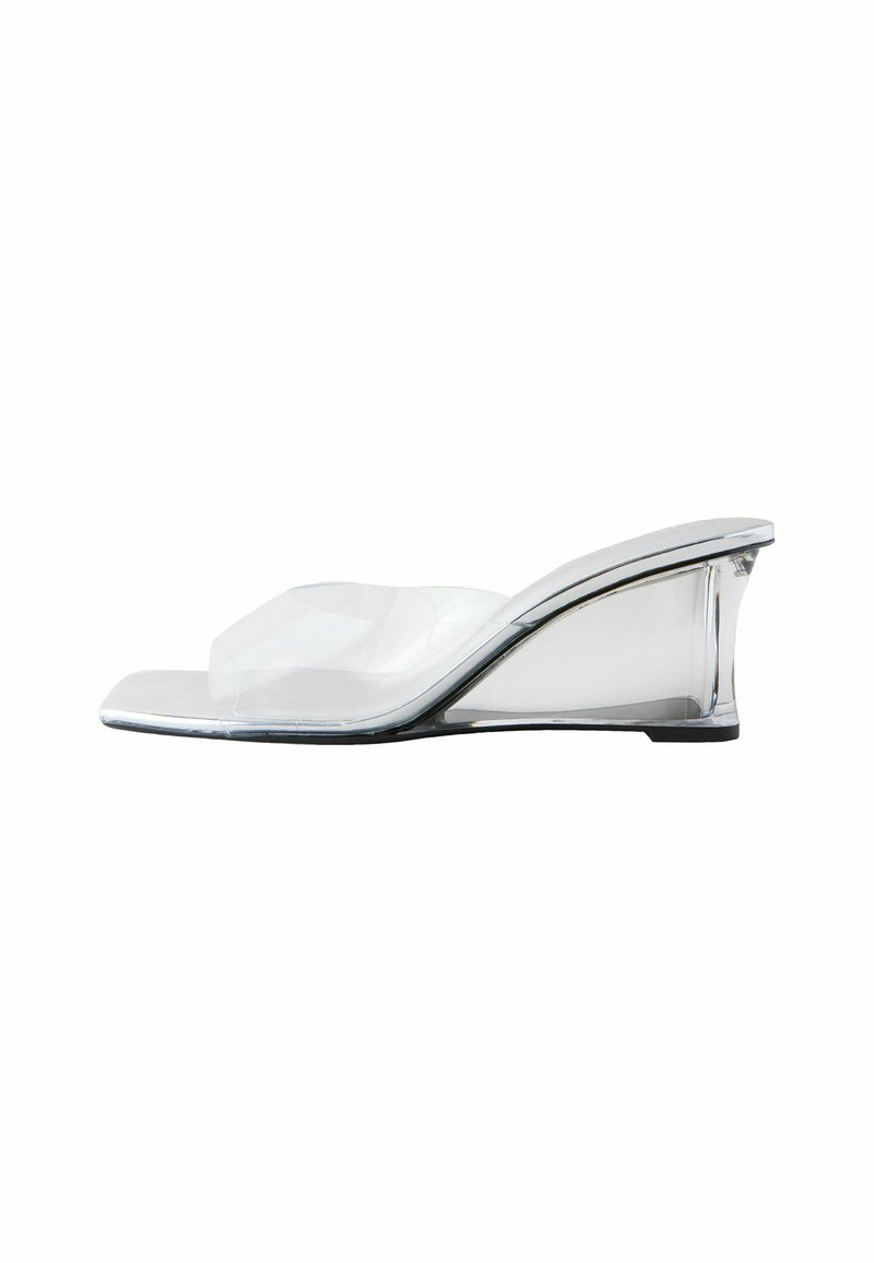 Sandale à talon compensé transparent avec une lanière incurvée et un design à bout carré, dotée d'un accent argenté brillant le long du bord de la semelle.