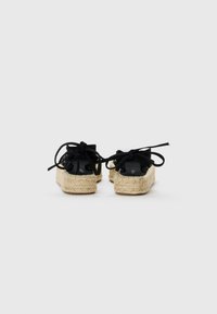 Espadrillas nere in tela con dettagli a fiocco, suole in corda di juta e fondi piatti in gomma beige, viste da dietro.