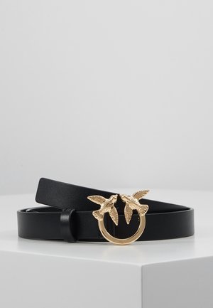 Schwarzer Ledergürtel mit goldener, runder Schnalle, die zwei detaillierte Vögel zeigt, die sich gegenüberstehen, auf einer weißen Oberfläche platziert.