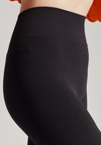 Czarne legginsy z wysokim stanem, wykonane z elastycznego materiału o gładkiej strukturze, z kątowymi szwami po bokach, co dodaje interesującego akcentu designowi.