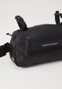 Black nylon waist bag with multiple zippered pockets, adjustable straps, and reinforced bottom. Features PeakPerformance logo and a compact design.