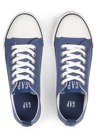 Zapatillas de lona color navy con punteras y cordones de goma blanca, con un prominente logotipo de "GAP" en la lengua y la plantilla. Diseño plano y de perfil bajo.