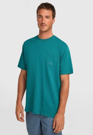 T-shirt a maniche corte color verde teal realizzata in tessuto morbido, con una tasca sul petto a sinistra con un logo. Vestibilità casual, scollo rotondo, design minimalista.