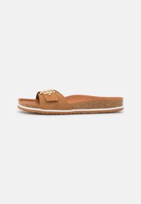Sandales à glissière en suede marron avec une large sangle, des accessoires décoratifs en or, et une semelle rembourrée semblable à du liège, accentuée d'une rayure blanche.