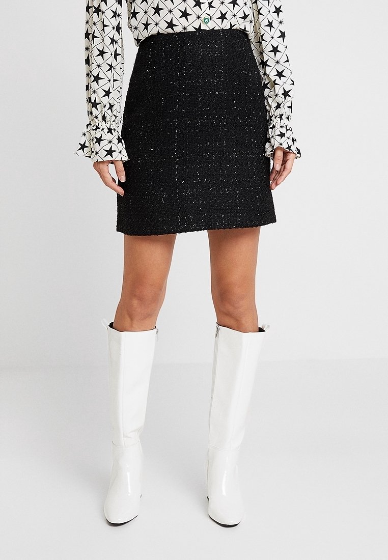 Svart tweed minikjol med texturerat tyg, i rak form. Kombinerad med vita knähöga blanka stövlar och en mönstrad blus.