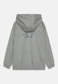 Siva dukserica s kapuljačom od mekog materijala. Ima veliki reflektirajući Nike logo na leđima i elastične manžete na rukavima.