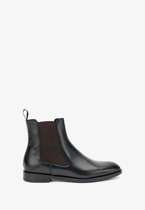 Bottine Chelsea en cuir noir avec panneaux élastiques sur les côtés, bout rond et une languette. Semelle plate, texture lisse, design minimaliste.