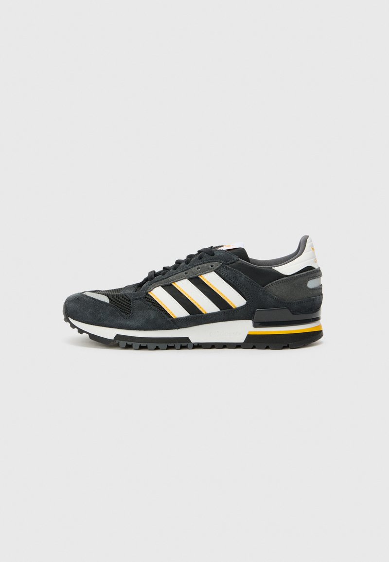 Black suede sneaker with white and yellow accents, featuring three stripes, a mesh toe, and a textured rubber sole. Classic athletic design.