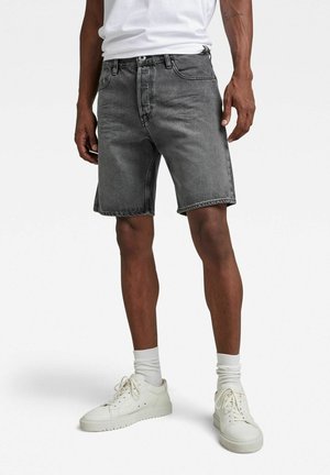 Shorts en denim gris avec une coupe classique, dotés de cinq poches et d'une fermeture par bouton. Associés à des baskets blanches et des chaussettes.