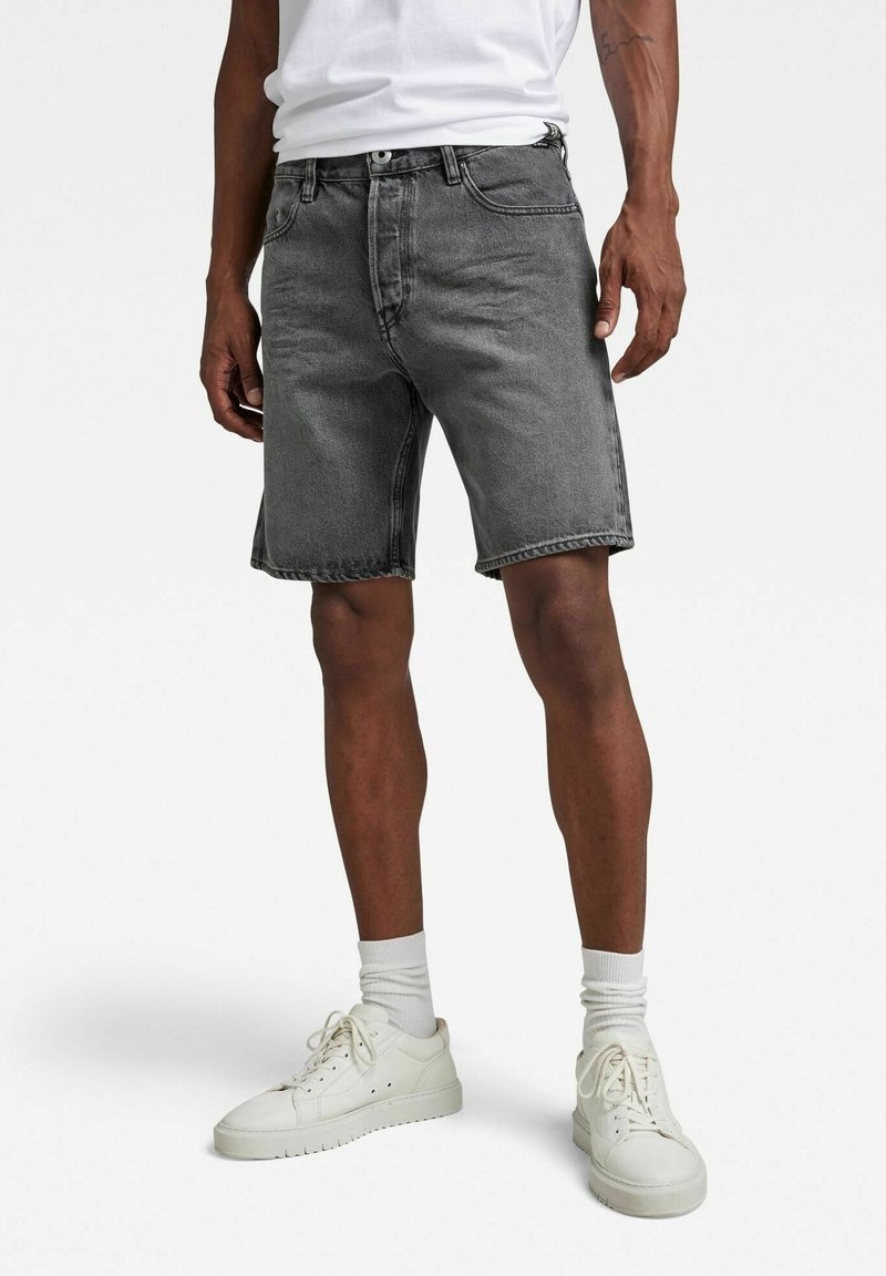 Shorts en denim gris avec une coupe classique, dotés de cinq poches et d'une fermeture par bouton. Associés à des baskets blanches et des chaussettes.