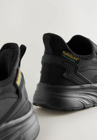Baskets noires imperméables avec une texture en tissu, bout rond, col rembourré et logo HydroGuard® visible sur le talon.