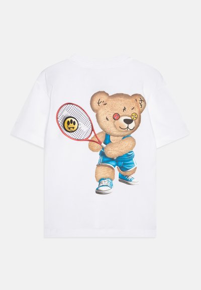 Camiseta blanca de manga corta con un oso de dibujos animados sosteniendo una raqueta de tenis roja, vistiendo pantalones cortos azules y zapatillas, con ojos de botones coloridos.