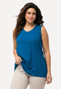 Top senza maniche blu con scollatura a V, realizzato in materiale morbido, con una vestibilità comoda e un orlo arrotondato. Abbinato a pantaloni beige chiaro.