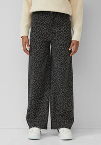 Zwarte denim broeken met wijde pijpen en een grijze luipaardprint. Gemaakt met een hoge taille en gecombineerd met witte sneakers en een crèmekleurige trui.