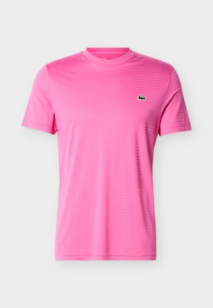 T-shirt rose à manches courtes avec col rond et petit logo crocodile vert sur le côté gauche de la poitrine, design sobre, présenté sur un fond gris.