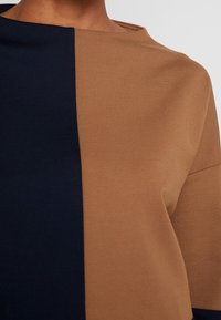 Top con bloques de color que presenta una textura suave, con azul marino oscuro a la izquierda y marrón claro a la derecha; escote recto y mangas cortas.