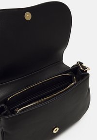 Sac à main en cuir noir avec des accents en métal doré. Il dispose d'un compartiment intérieur zippé et d'une fermeture à pression magnétique en haut.