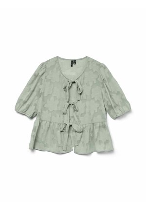 Blouse vert clair avec motif floral texturé, manches courtes à volants et fermeture à nouer à l'avant. Détail de l'ourlet peplum évasé.