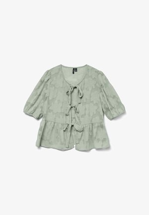 Blouse vert clair avec motif floral texturé, manches courtes à volants et fermeture à nouer à l'avant. Détail de l'ourlet peplum évasé.