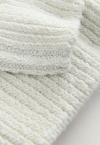 Paksu valkoinen neulekangas, jossa on ribattu pinta ja erottuvat ompeleet. Pehmeä villamateriaali, jossa on näkyviä kuituja ja hieman pörröinen pinta.