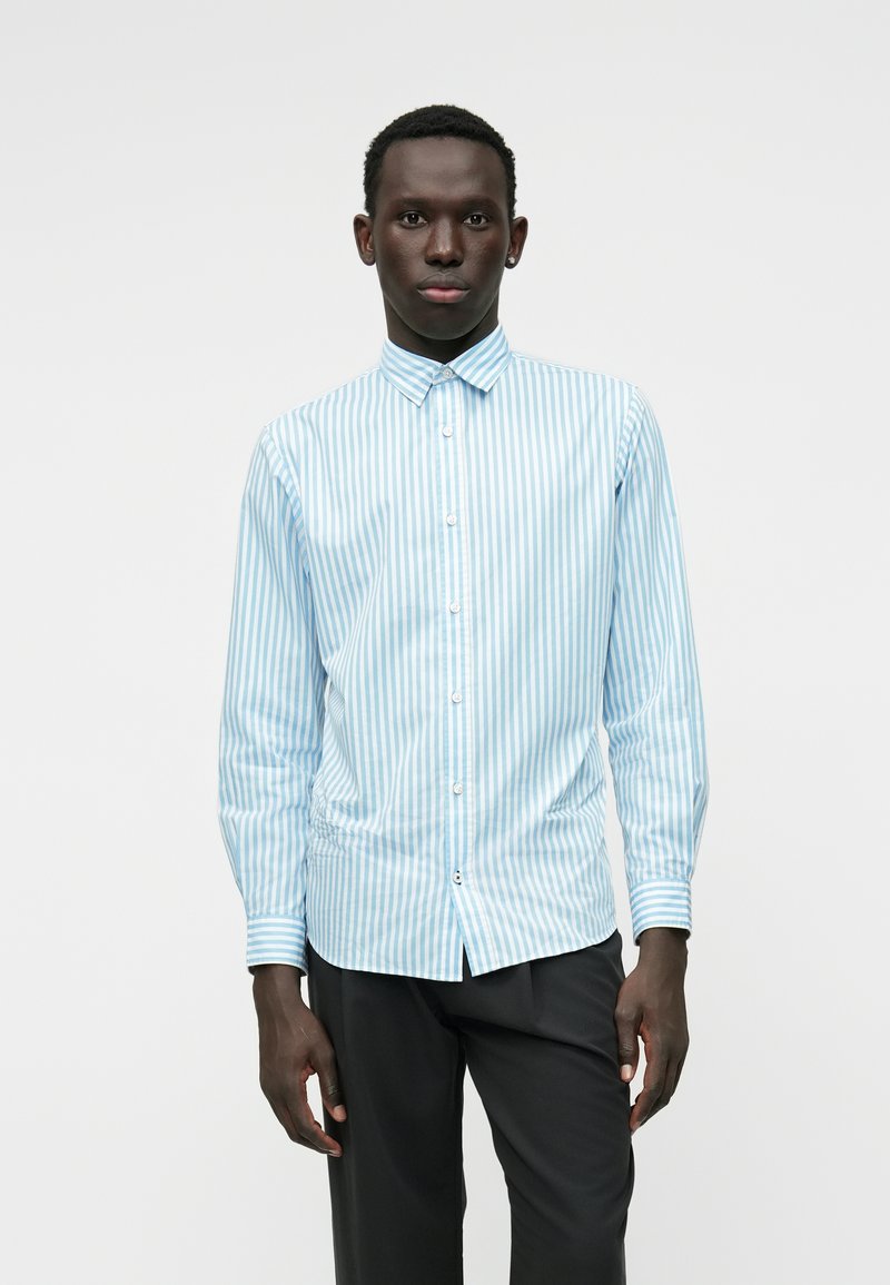 Camicia a maniche lunghe striata blu chiaro e bianca, con colletto, chiusura con bottoni e polsini aderenti. Tessuto dalla trama liscia.