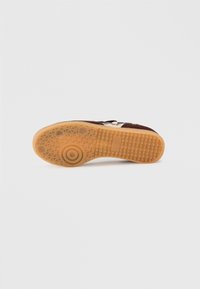Talpa de sneaker din suede maro cu o bază din cauciuc de gumă. Prezintă un model circular și o suprafață texturată pentru aderență, sporind tracțiunea și durabilitatea.
