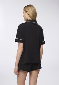 Pigiama nero a maniche corte con colletto e dettagli in piping bianco, abbinato a pantaloni corti neri coordinati, caratterizzati da una consistenza morbida e liscia.