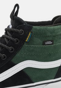 Sneakers Vans high-top in suede nero e verde, con strisce laterali bianche, lacci neri e un'etichetta con la scritta "HydroGuard" e "VANS."