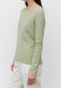 Lichtgroene ribbeltrui met lange mouwen, een ronde hals en een ontspannen pasvorm, gecombineerd met lichtgekleurde broek. Heeft een gestructureerde afwerking.