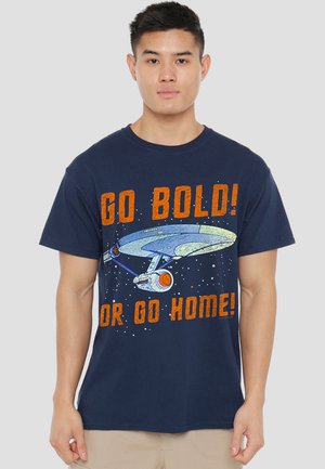 Navy t-shirt featuring an illustration of a spaceship against a starry background. Text reads “GO BOLD! OR GO HOME!” in orange font.