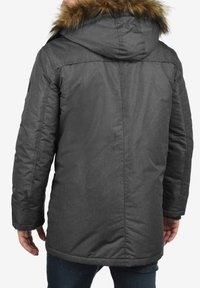 Grå isoleret parka med en hætte kantet med pels, der har et struktureret stof og en knælængde, detaljeret syning og sidelommer.